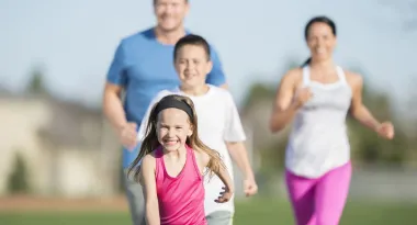 An image of a Caucasian family consisting of a young girl, teenage boy, and a mom and dad captured on a family run on a sunny day on the outdoor track of their local YMCA.