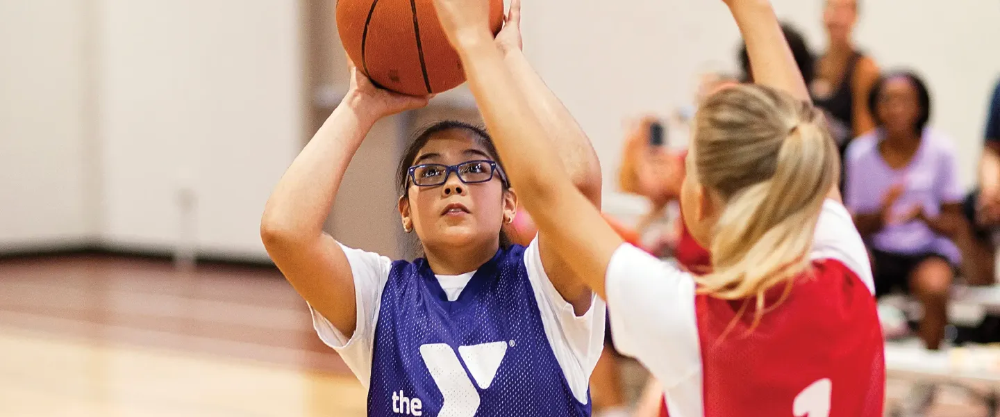 A young YMCA sports participant shoots a basketball goal during a YMCA Youth Basketball game