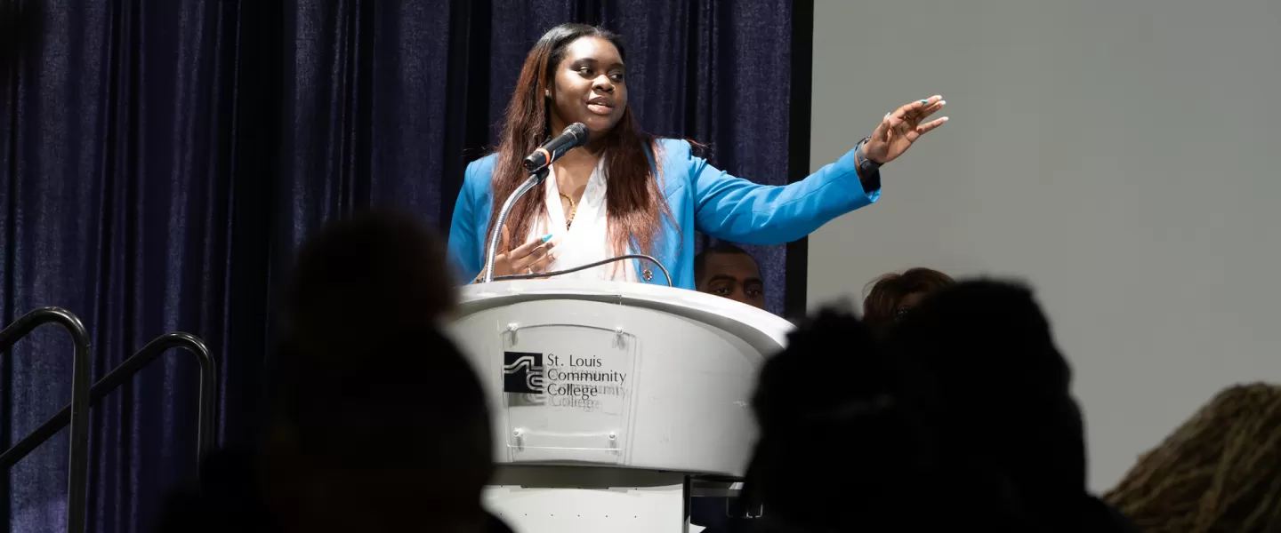 Student Delivering a Speech – A young participant confidently speaks into a microphone at a podium, addressing peers during a formal debate session.