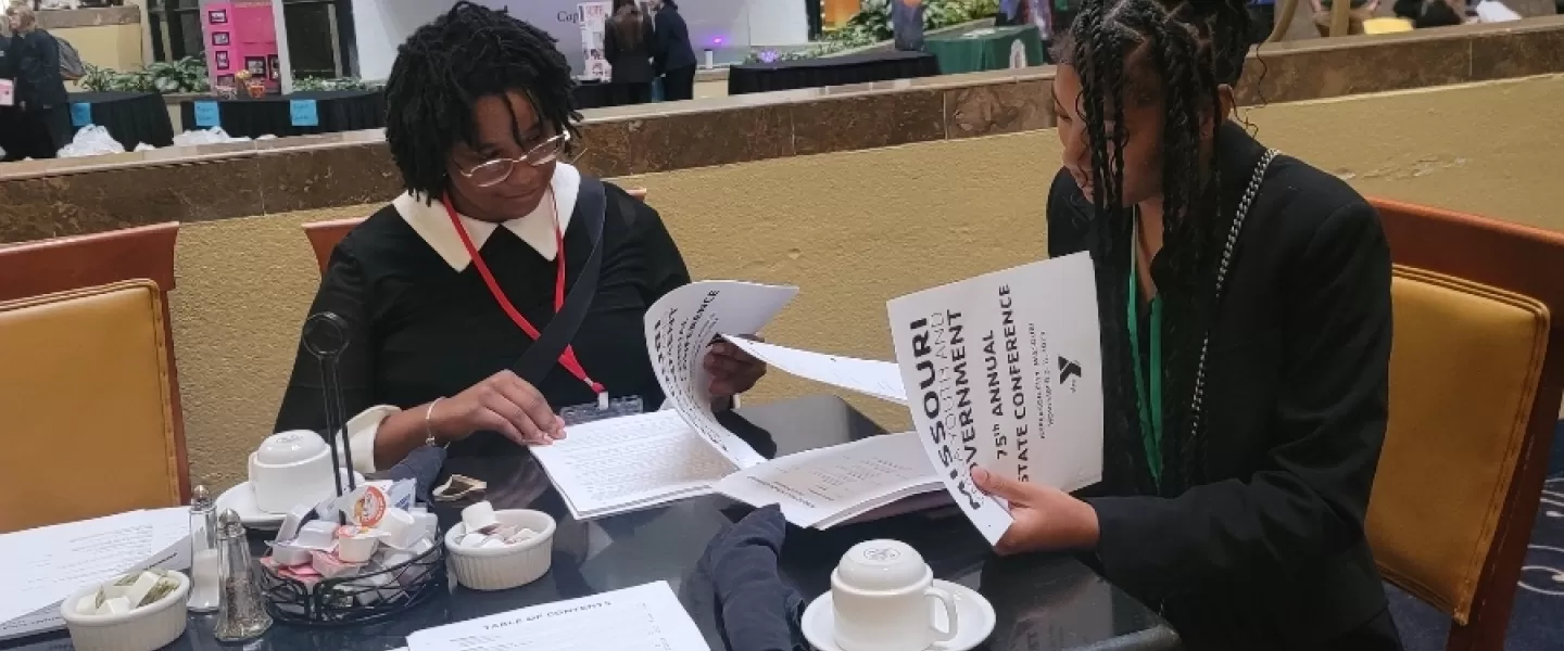 Collaboration with Law Students – A Missouri Judge leans over a table, helping high school students refine their ordinances with legal guidance. Papers and law books are spread across the table.