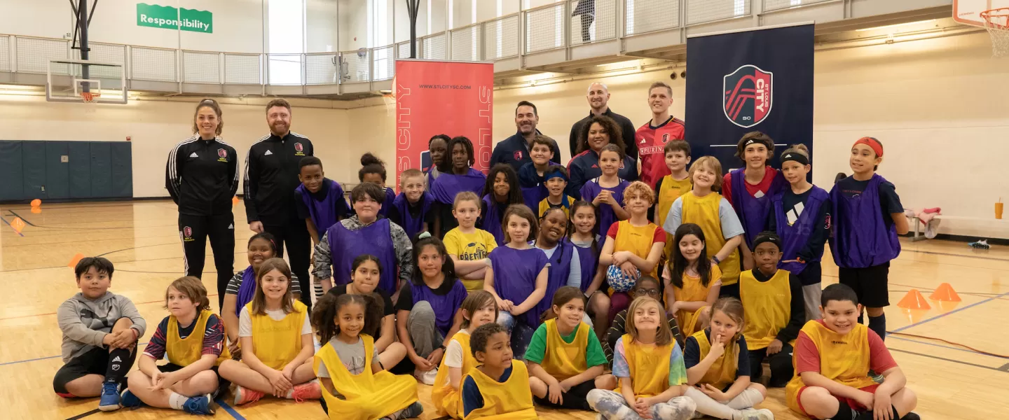 St. Louis CITY SC players, leadership staff, and Gateway Region YMCA representatives stand together at the City SC Kickoff event, celebrating the launch of the youth soccer program.