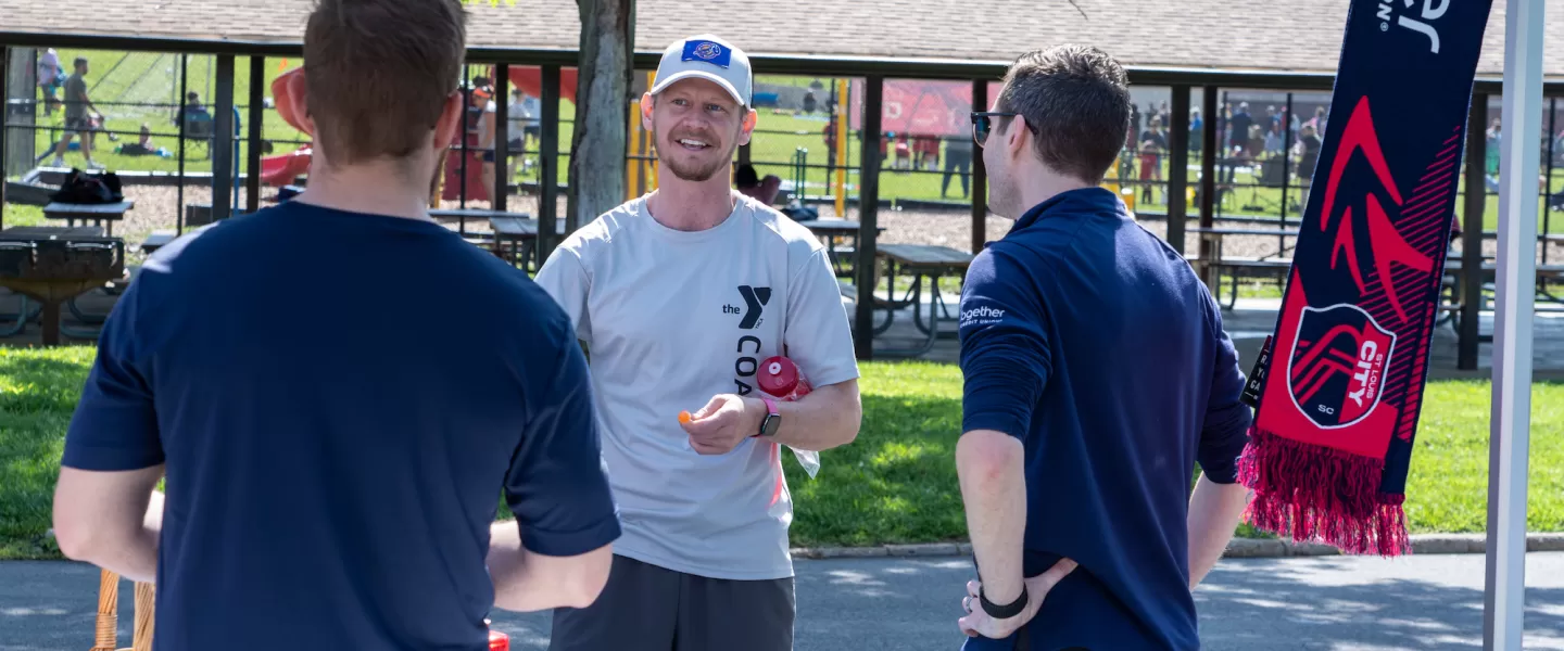 A YMCA Youth Soccer coach at the CITY SC Kickoff event smiles while engaging with young players, helping to lead drills and encourage participation.