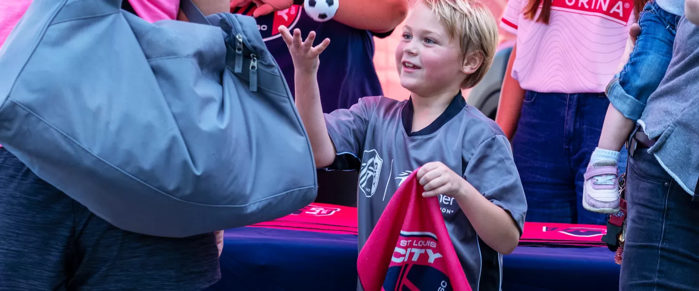 A young boy at the CITY SC Kickoff event proudly holds CITY SC swag, smiling as he celebrates the new youth soccer partnership with the Gateway Region YMCA.