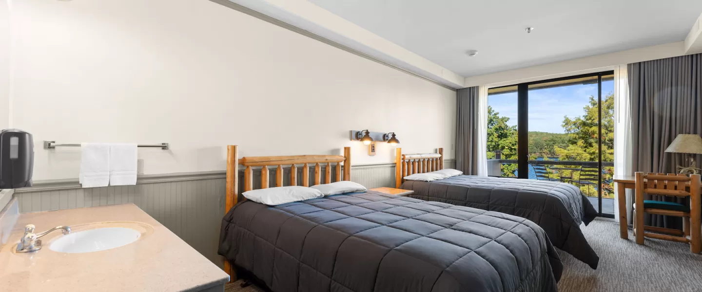 Wide view of Trout Lodge Room with two queen beds, dresser, and lake-facing patio doors