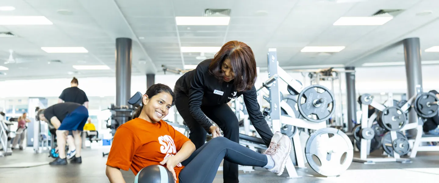 A certified YMCA Personal Trainer helps her client through a bodyweight exercise with a medicine ball