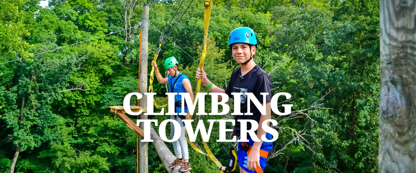 A camper in a safety harness climbing up the high wooden climbing tower.