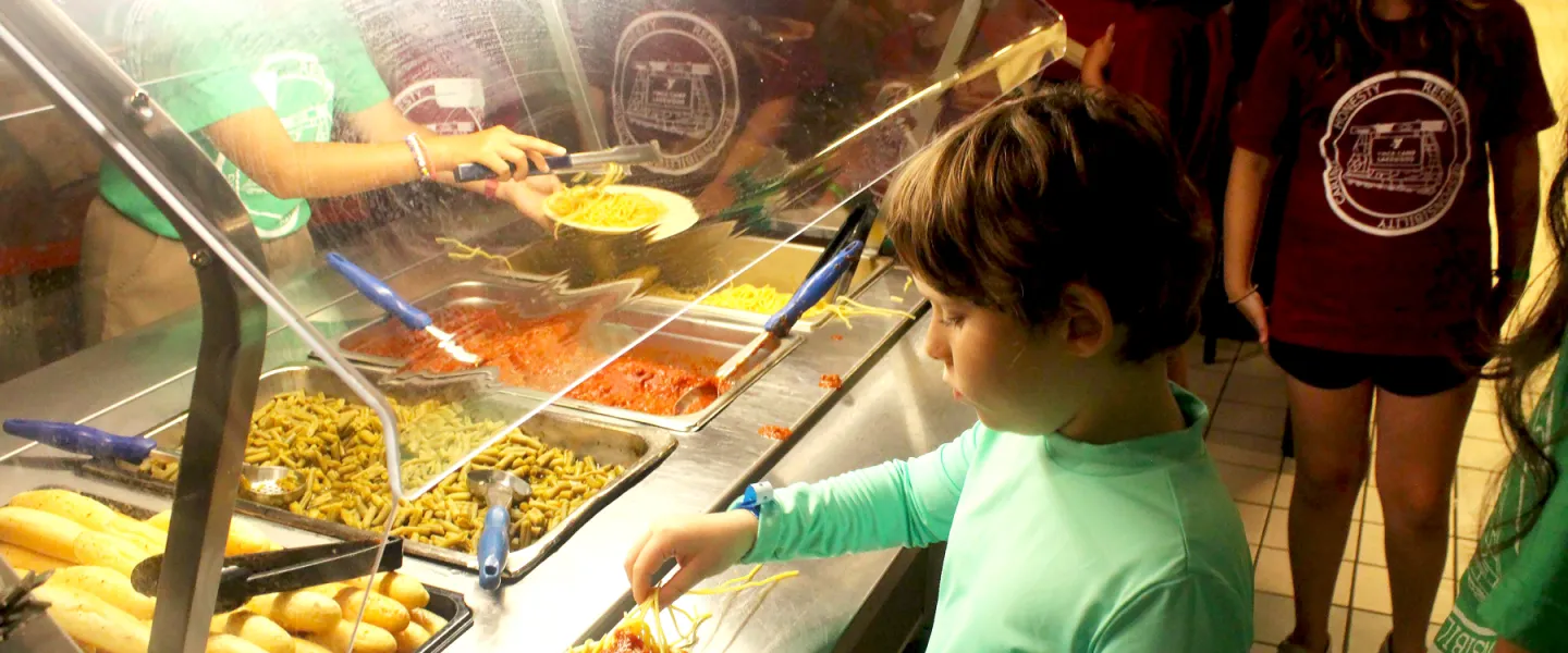 Campers lining up to serve themselves hot pasta and sauce from the buffet-style serving line.