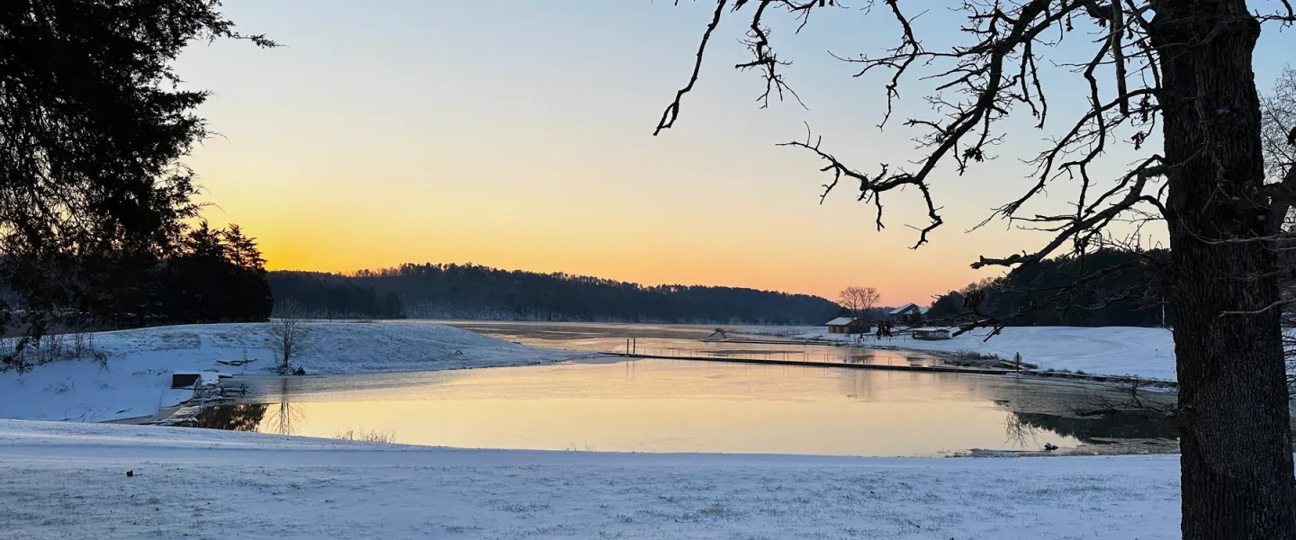 Panoramic view of frozen Sunnen Lake surrounded by snow-covered Ozark hills at sunset at YMCA Trout Lodge.