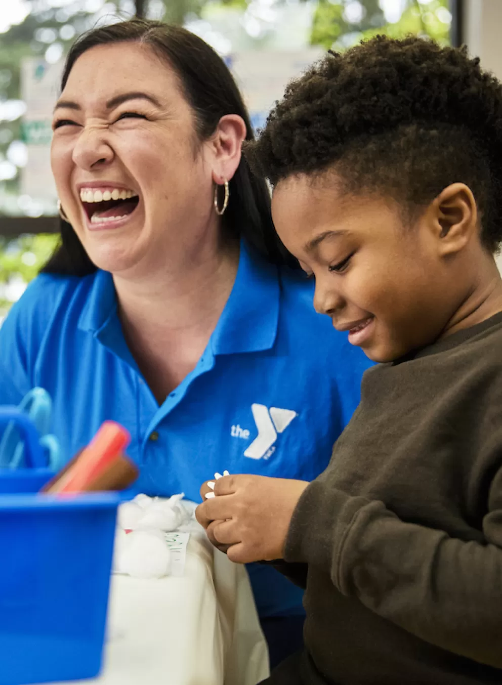 A YMCA Staff member and children laugh during a craft project in Child Watch
