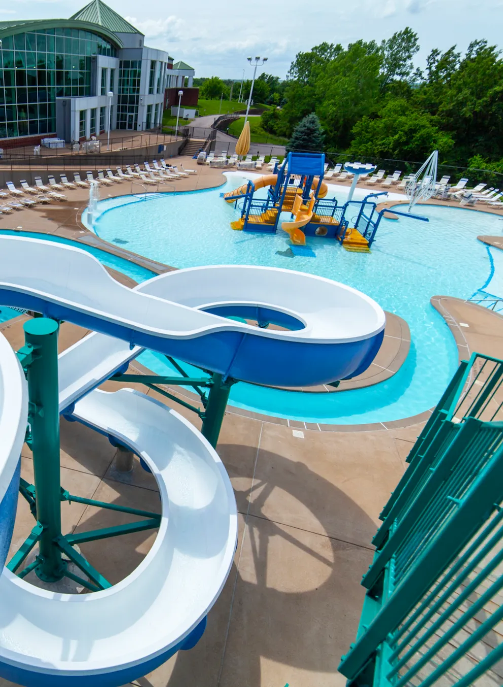 RiverChase YMCA Gym Fenton, MO Outdoor Aquatic Center featuring a water slide, lazy river, zero-depth entry pool, kiddie splash pad and play structure, and lap pool.