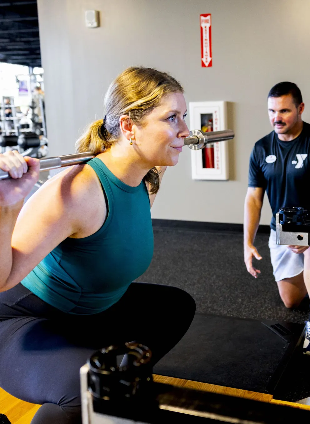 A certified YMCA Personal Trainer assists a ymca member with a deadlift squat with a plate weight bar.