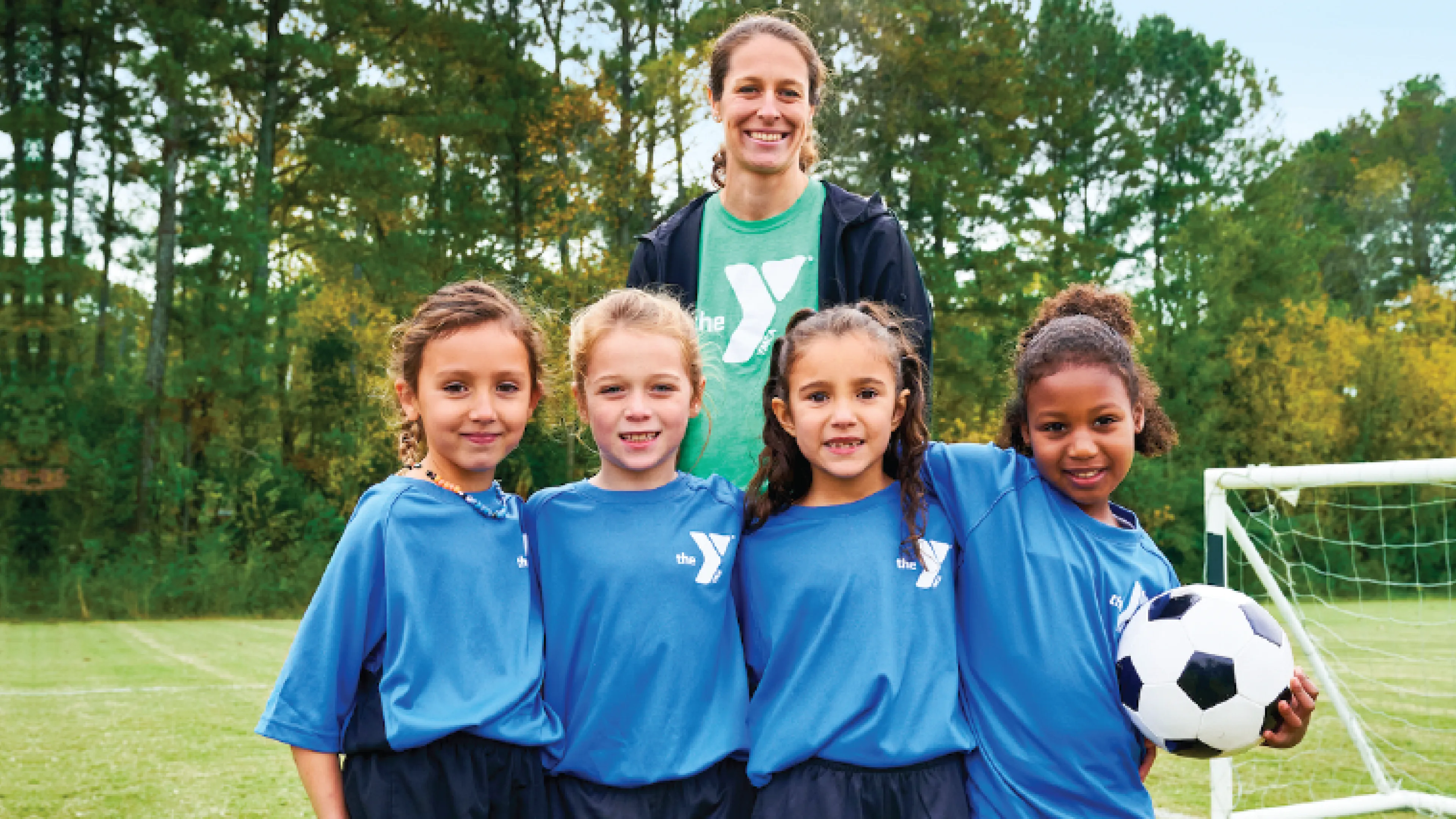 a ymca youth soccer volunteer coach smiles with her girls youth soccer team