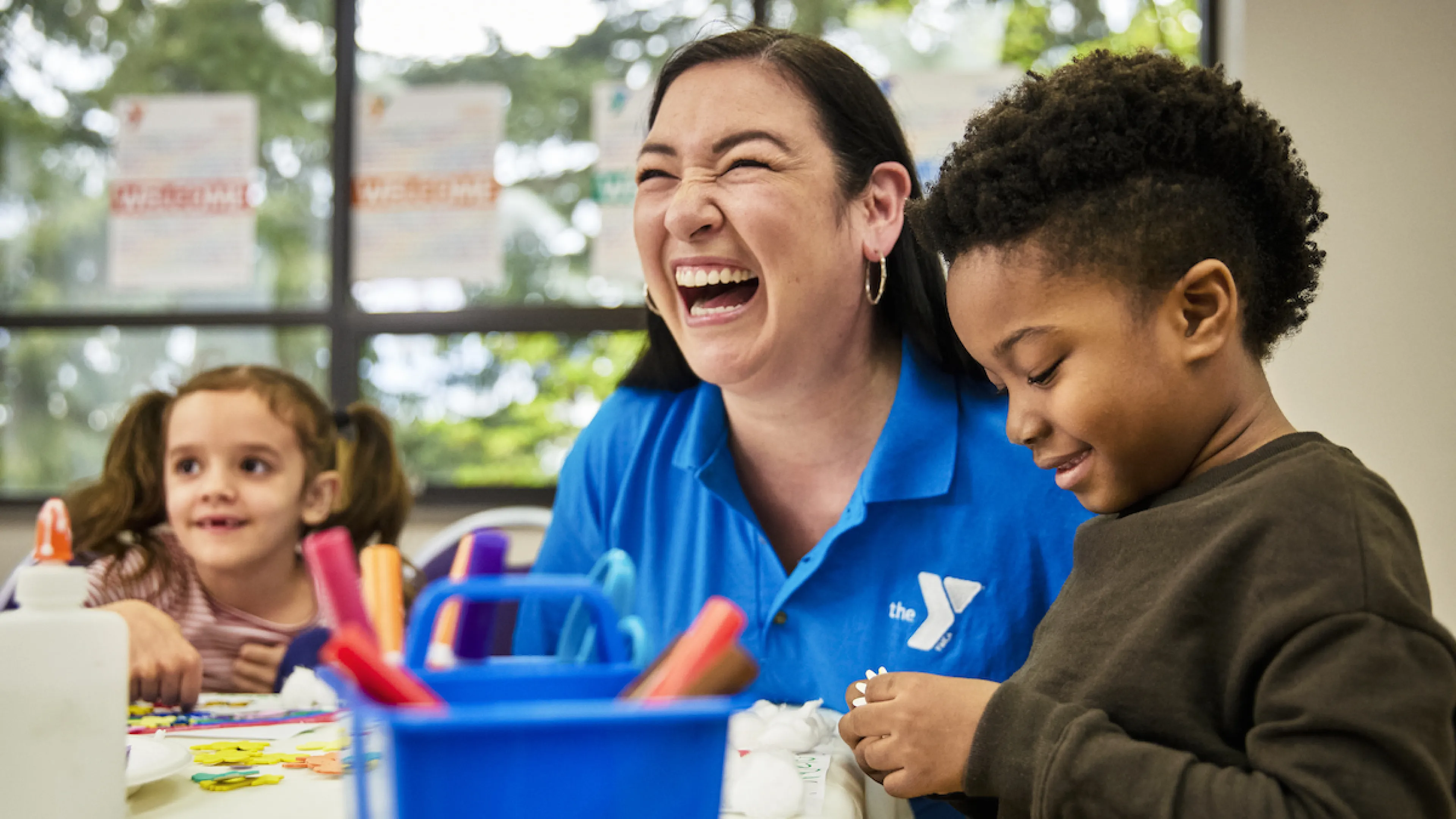 A YMCA Staff member and children laugh during a craft project in Child Watch