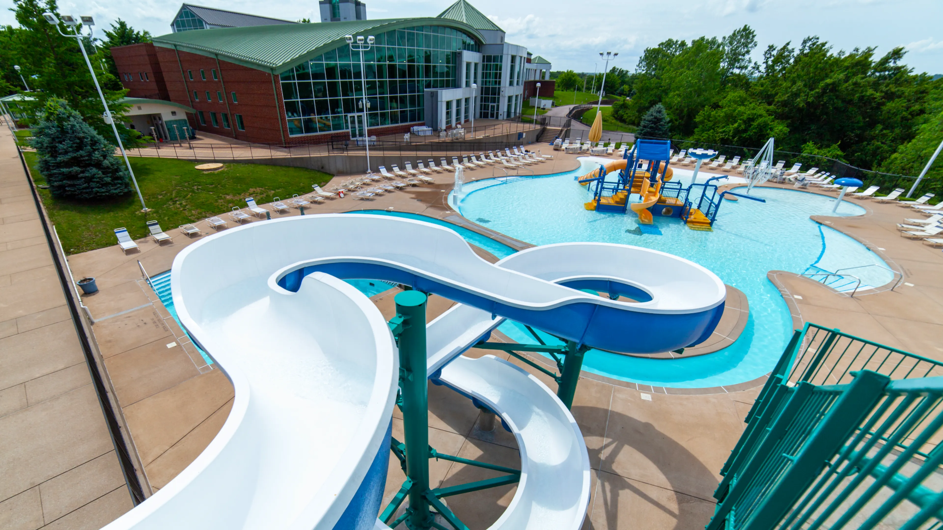 RiverChase YMCA Gym Fenton, MO Outdoor Aquatic Center featuring a water slide, lazy river, zero-depth entry pool, kiddie splash pad and play structure, and lap pool.