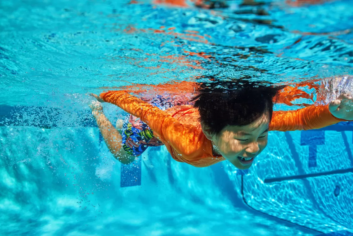 Child swimming underwater in a YMCA outdoor swimming pool with clear blue water.