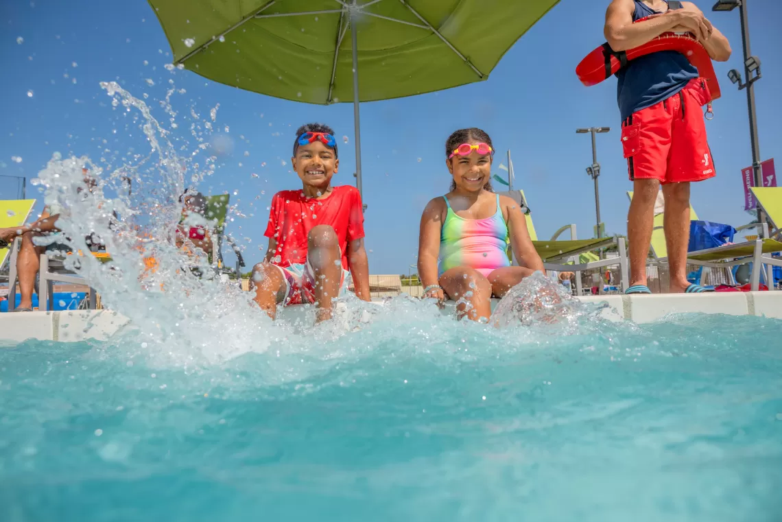 Two children paired up with the "buddy system" splash by the side of a YMCA Outdoor Pool supervised by a YMCA Lifeguard