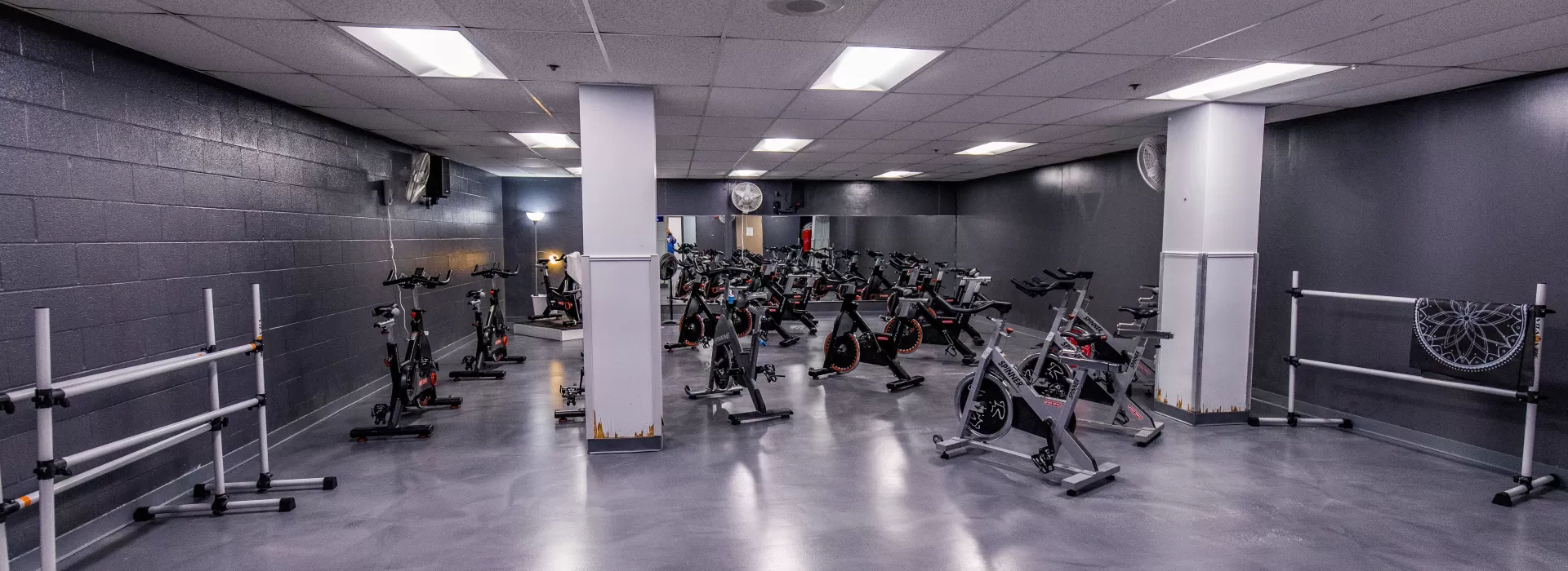 Cycling room with spin bikes placed throughout room. Industrial feel with concrete floor and grey walls.